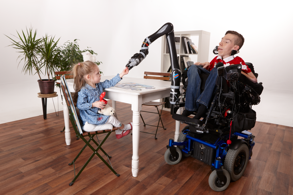 Man in a wheelchair with the Jaco Robotic Arm doing a puzzle with a little girl