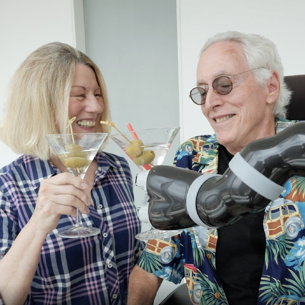 Bill Faia toasts with his wife, using his Jaco Robotic Arm that he's named Charlie