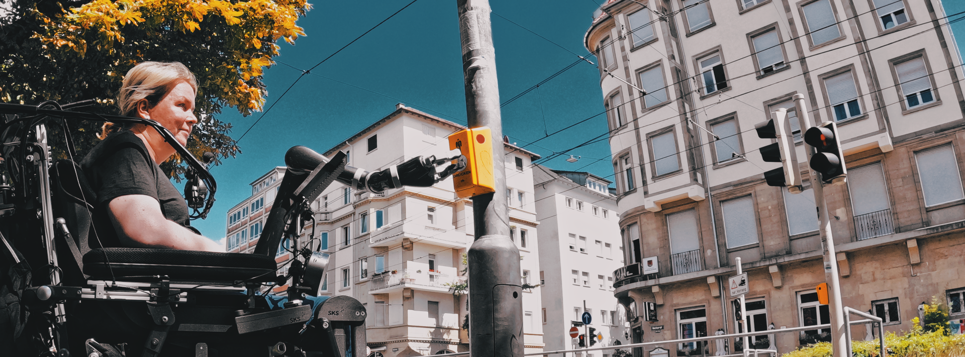 Woman uses Jaco to press a walk signal button at a crosswalk
