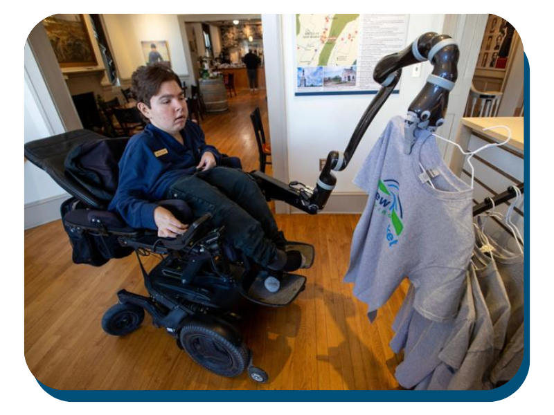Wade Custer uses a new robotic arm on his wheelchair to pick up a book in the New Market Battlefield Visitor Center Grabbing shirt